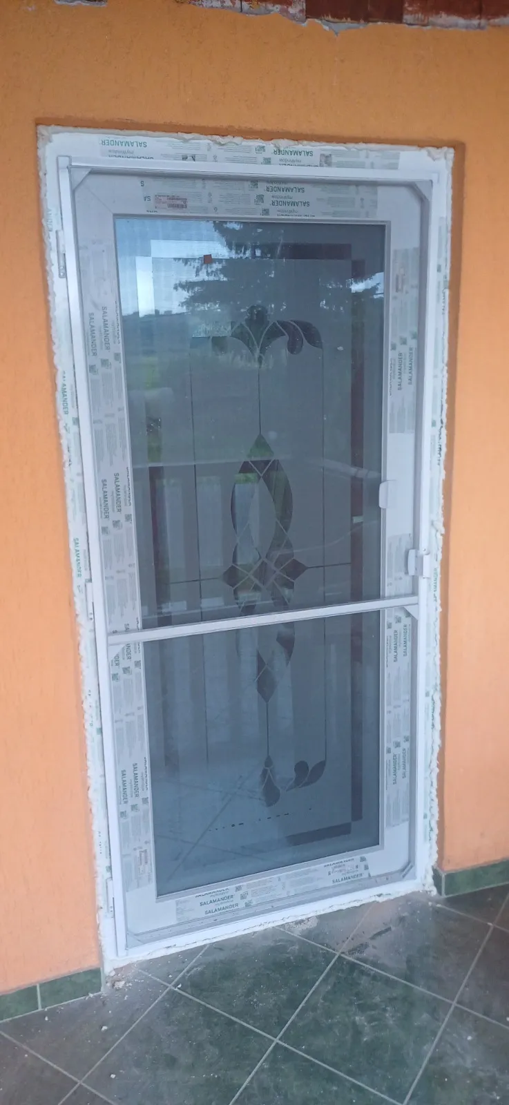 Ușă PVC albă cu geam decorativ la o intrare în curs de finisare