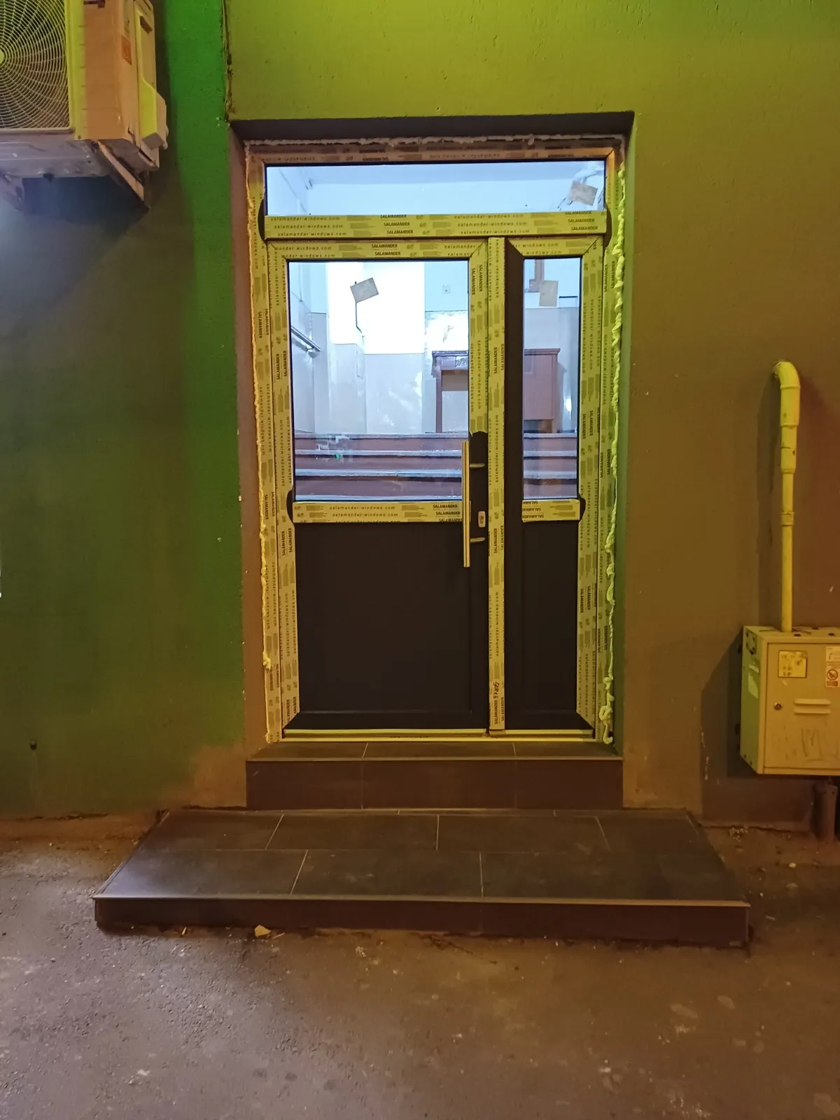 Intrare vitrată din aluminiu și PVC într-un spațiu cu pereți verzi